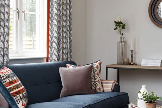 Lounge featuring Carnac dark indigo curtains with a red-lined edge, paired with a blue sofa. Design by Sims Hilditch.