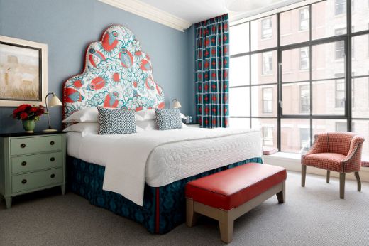 A Firmdale hotel room with a large bed featuring a colourful, patterned headboard designed by Kit Kemp using Christopher Farr Cloth Carnival fabric